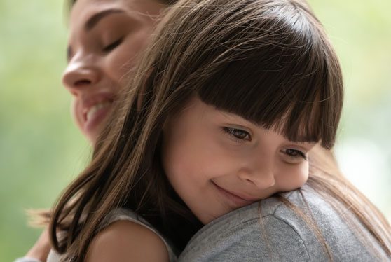 Side view close up head shot happy little adopted kid girl put head on mothers shoulder, feeling love and support. Small cute daughter hugging embracing cuddling young smiling mother at new home.