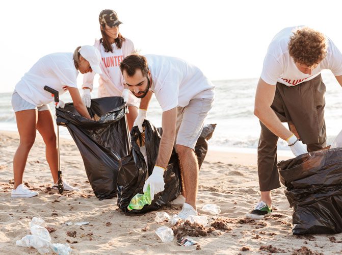 Photo of caucasian eco volunteers people cleaning beach from plastic with trash bags at seaside