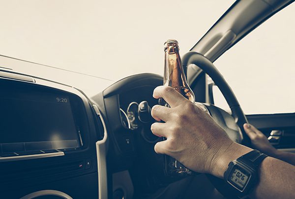 A driver holds a beer bottle to the wheel, hiding the label.