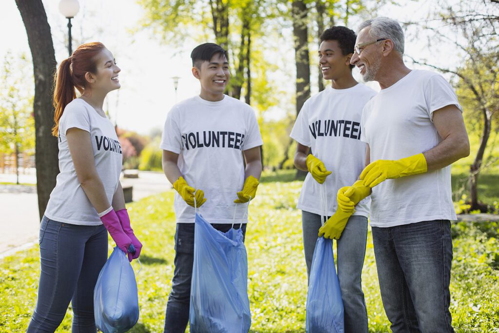 Volunteers in white t-shirts laugh with each other while they pick up debris outdoors.