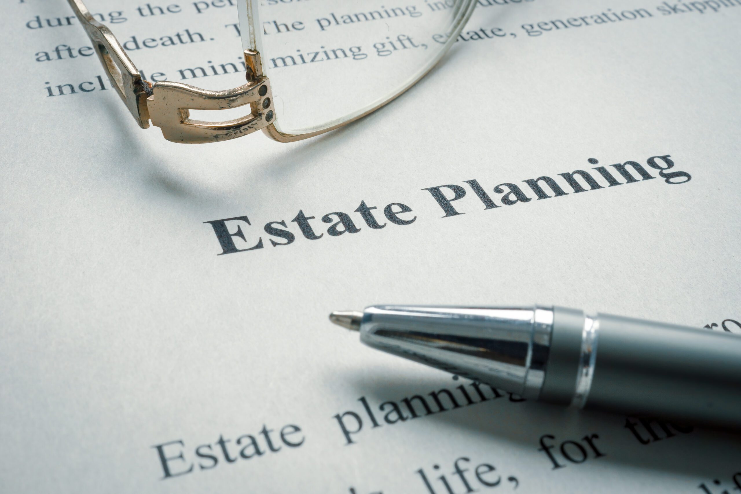 An image of a paper that says “estate planning” with glasses and a pen on top of the paper.