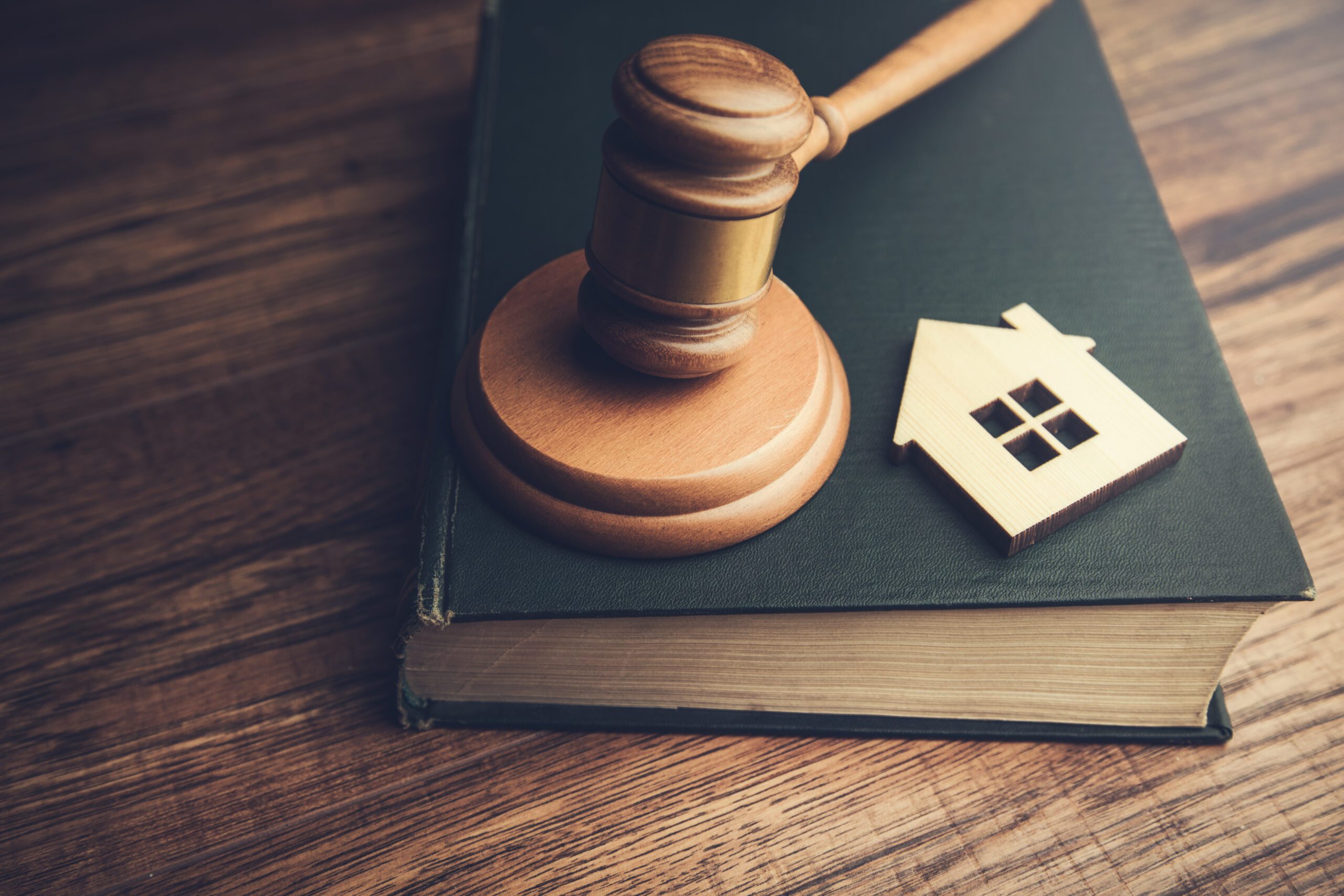 a gavel resting on top of an old, blue book with a small wooden cutout of a house next to the gavel