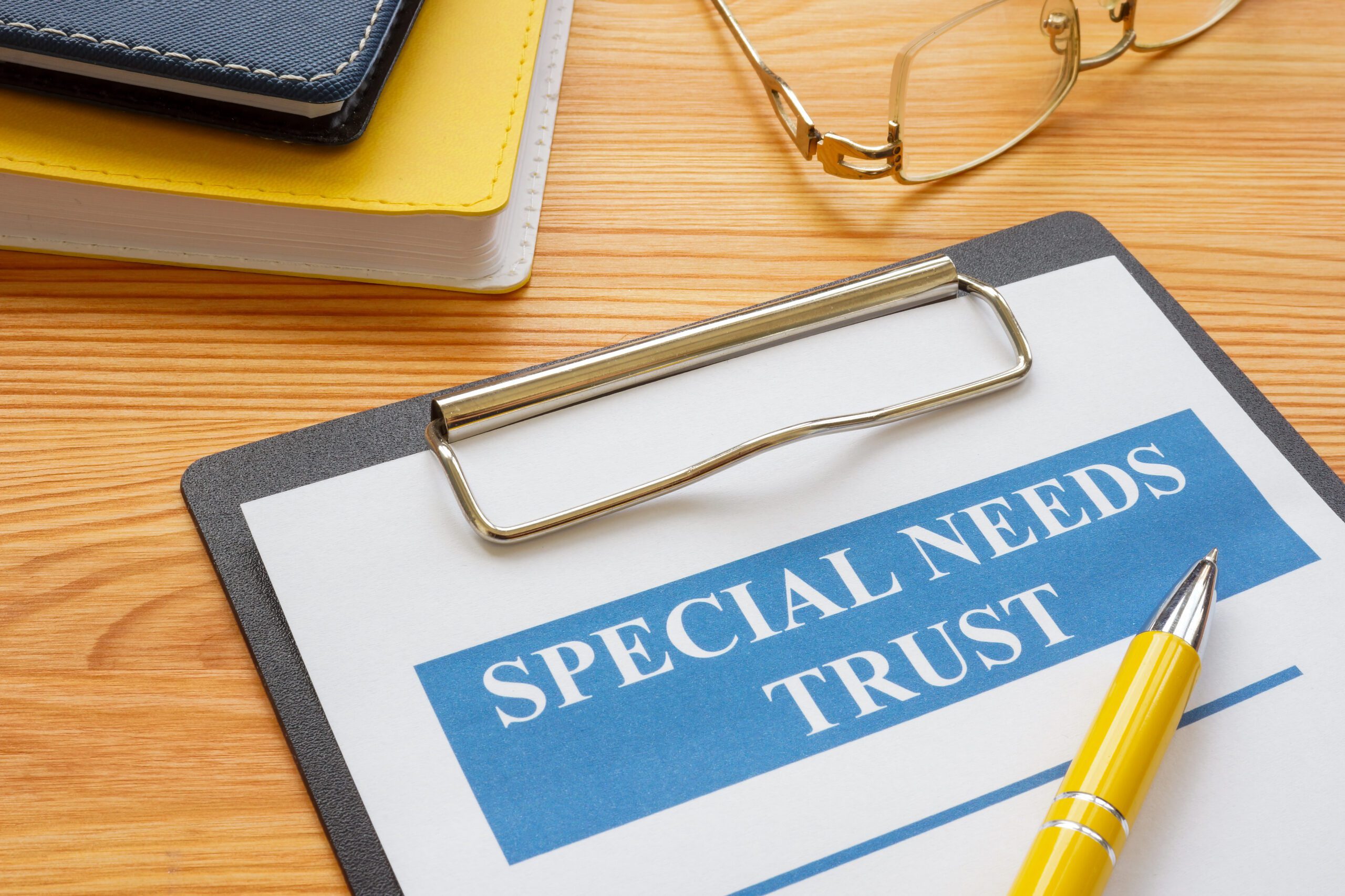 A clipboard on a desk with a sheet of paper on it with “special needs trust” written in white inside a blue text block.