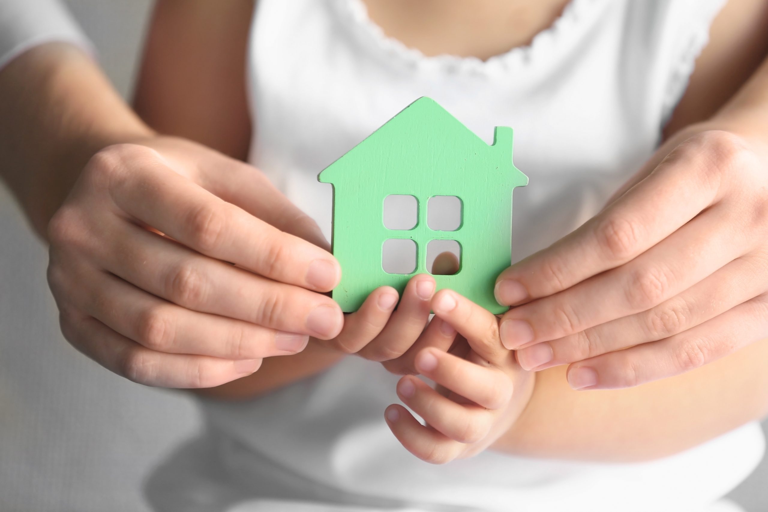 An adult and a child hold a small green home together in their joined, cupped hands.