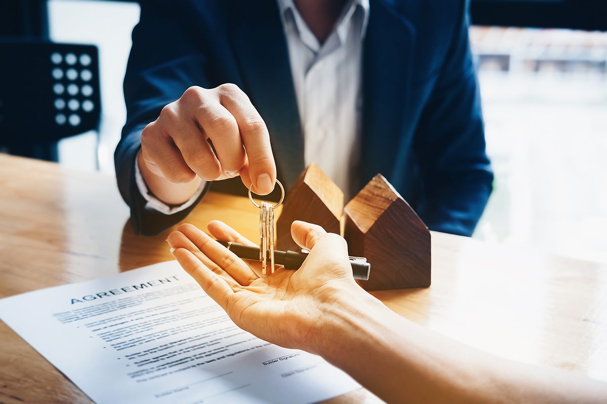 A person is receiving keys to a property with a pen in their hand and a contract on the table.