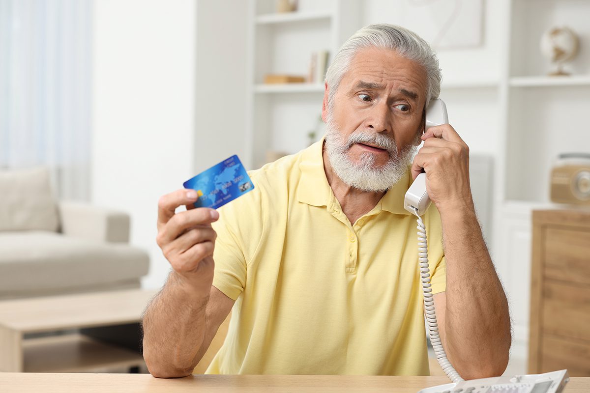 A man holding his credit card and talking on the phone with a concerned look on his face.