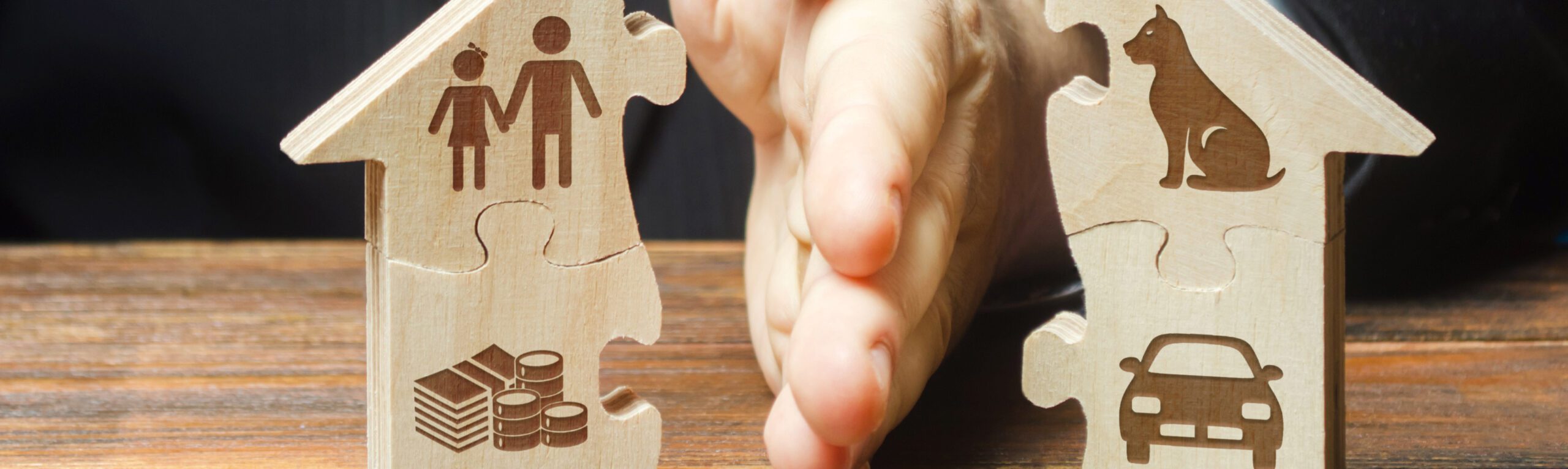 A person in a suit with a blue tie separates a puzzle home with their hand, symbolically splitting assets.