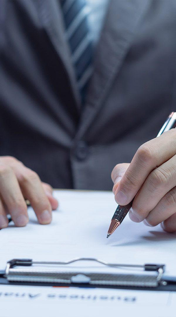 Businessman writing signature on contract at office desk, confirming agreement